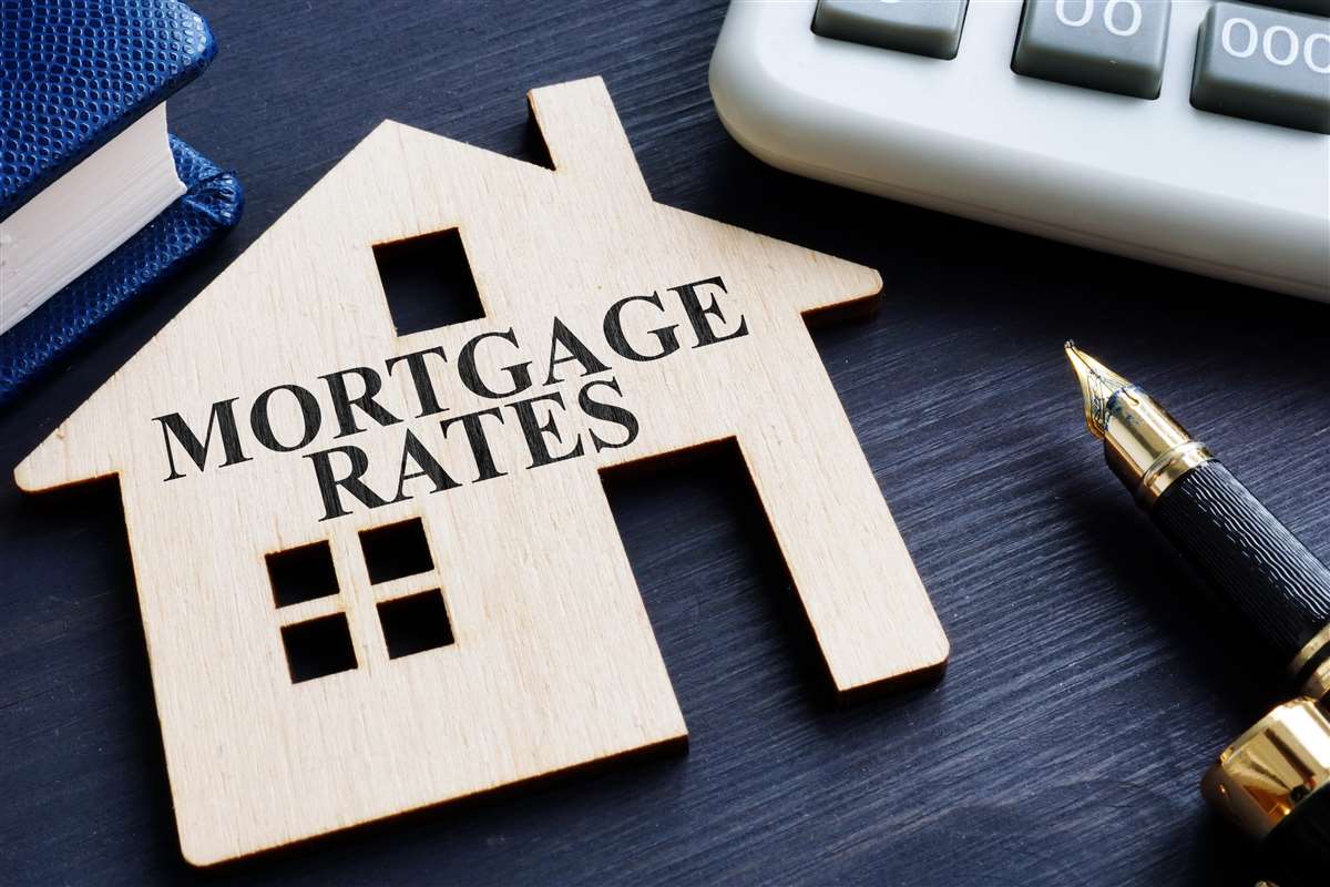 modellino di casa in legno con scritta mortgage rates, calcolatrice e penna