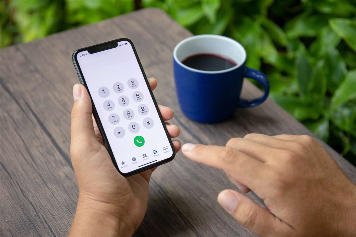 Persona che digita numero sul telefono, sullo sfondo una tazza di the