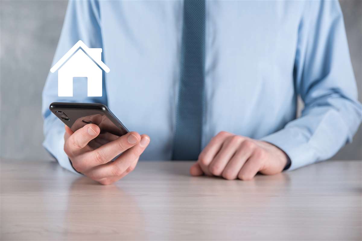 uomo tiene in mano uno smartphone dal quale esce l'icona di una casa