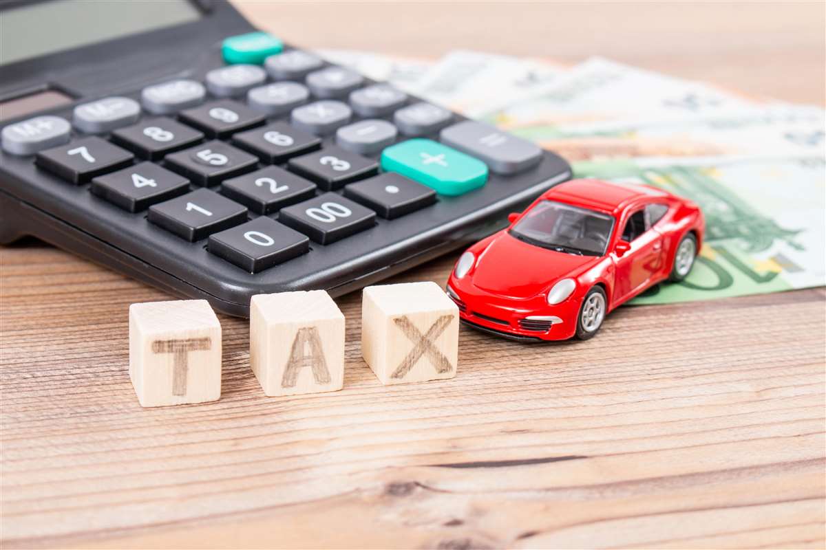 scritta tax su cubetti in legno vicino a modellino di auto, calcolatrice e banconota da 100 euro
