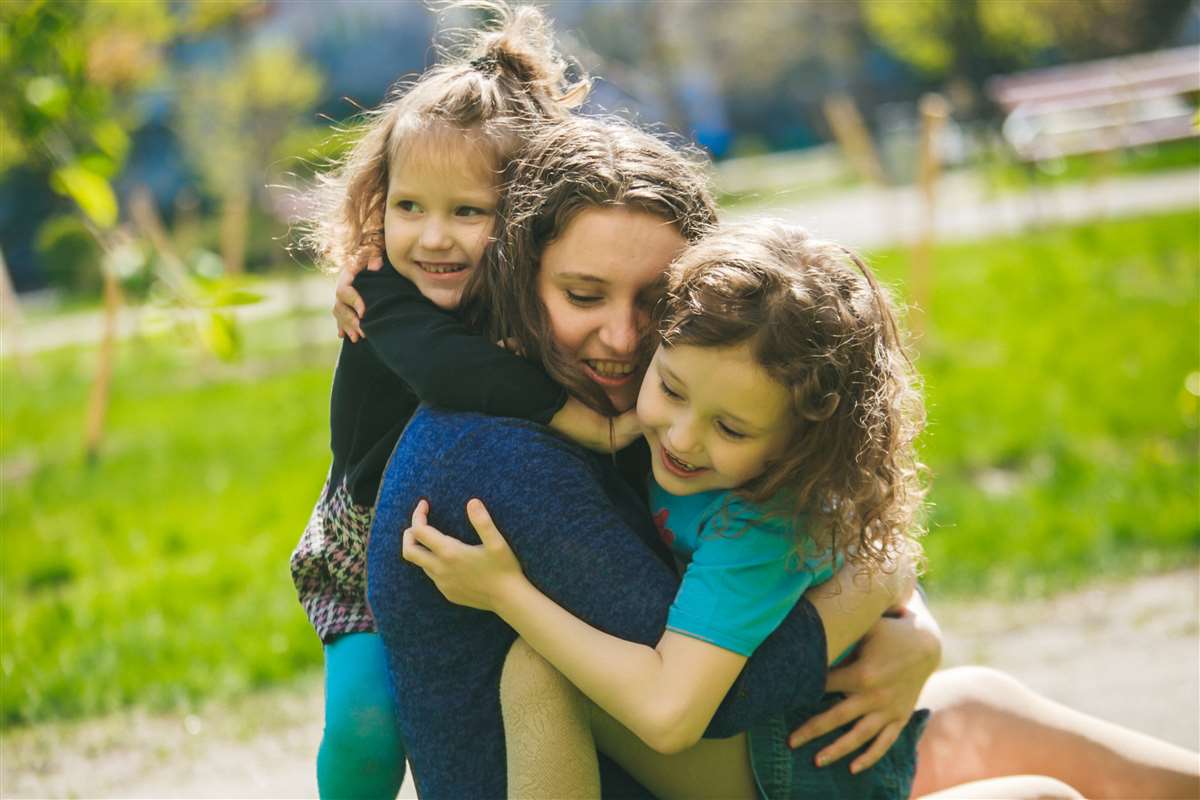bonus mamme due bambine abbracciano la mamma in un parco pubblico