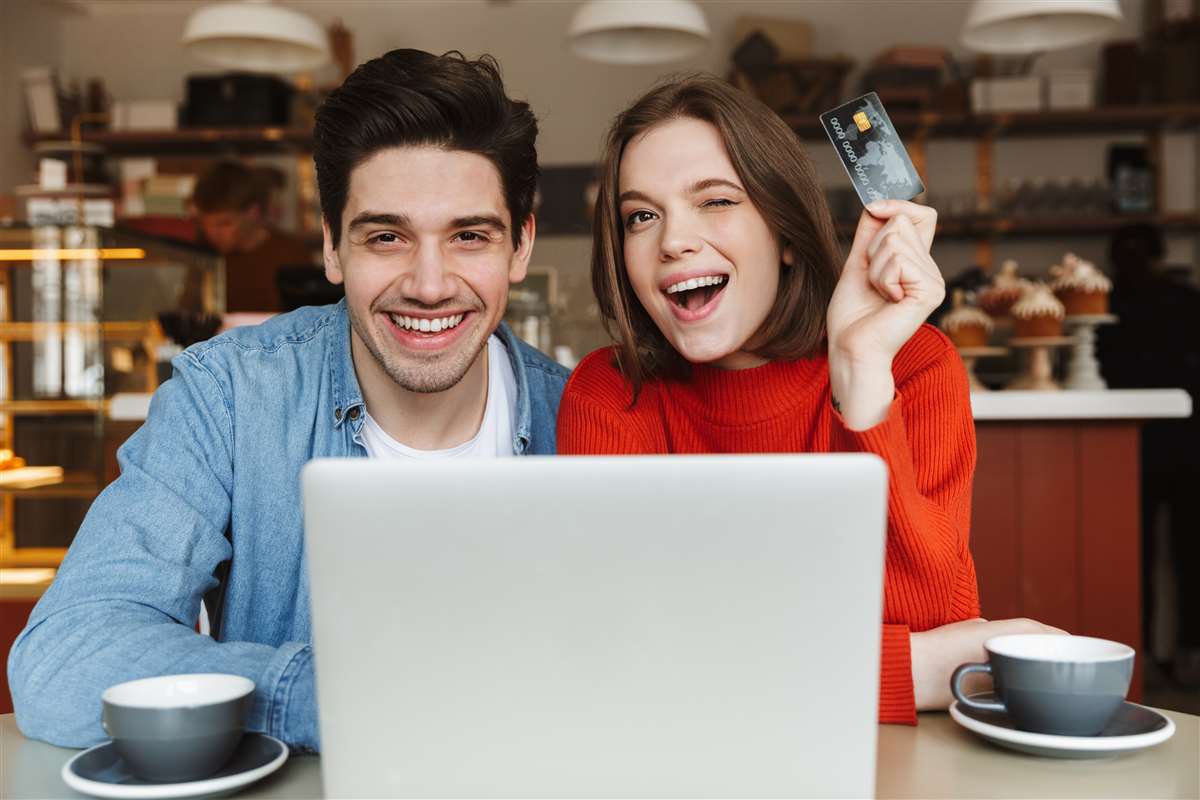 coppia sorridente al pc con carta di credito in mano