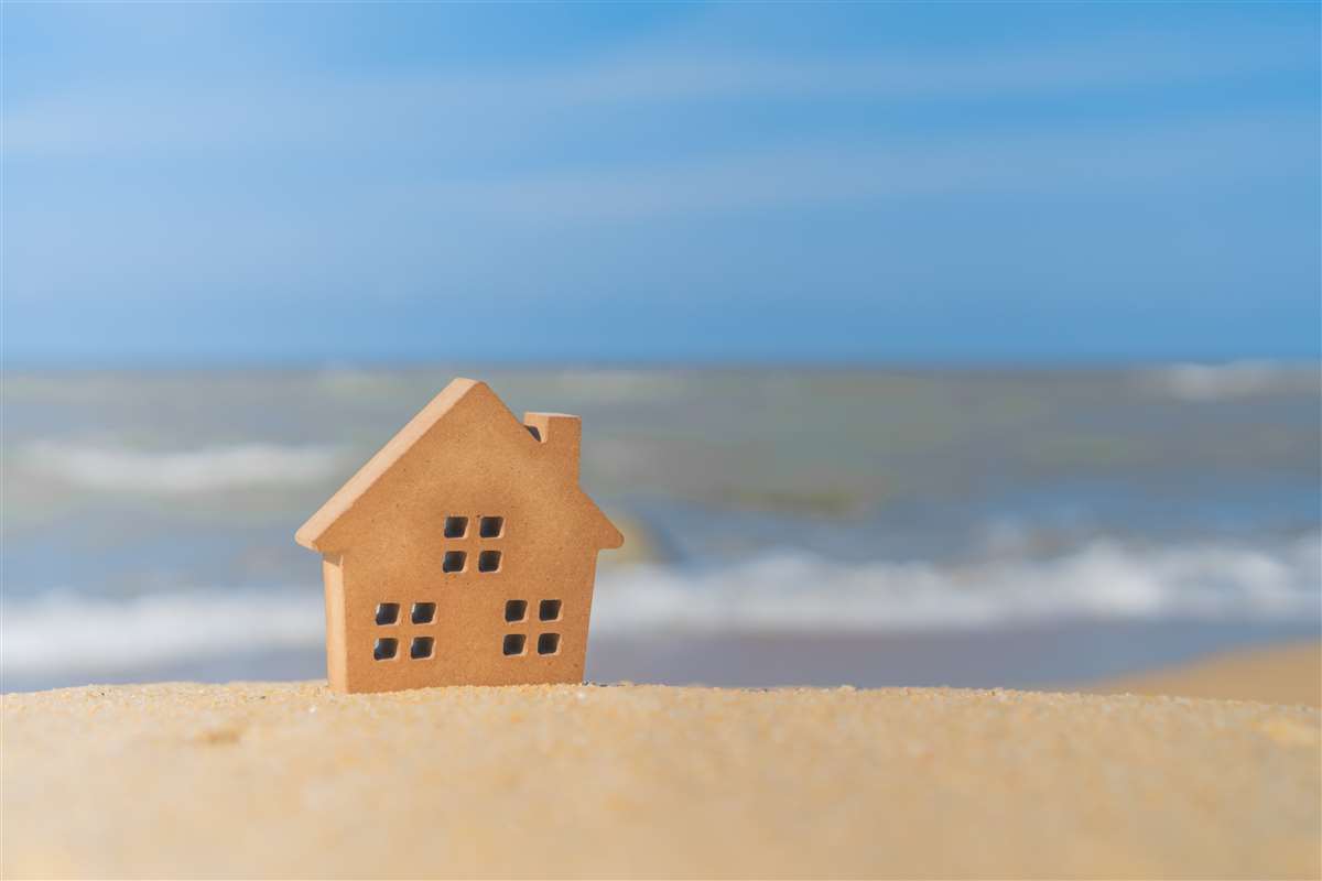 modellino di casa posizionata sulla spiaggia con mare come sfondo