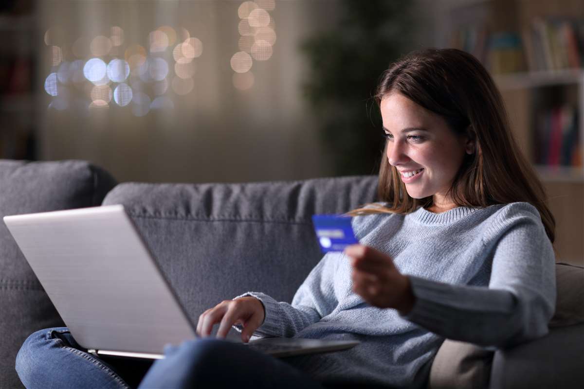 donna felice nella notte acquista online con carta di credito e laptop seduto su un divano a casa