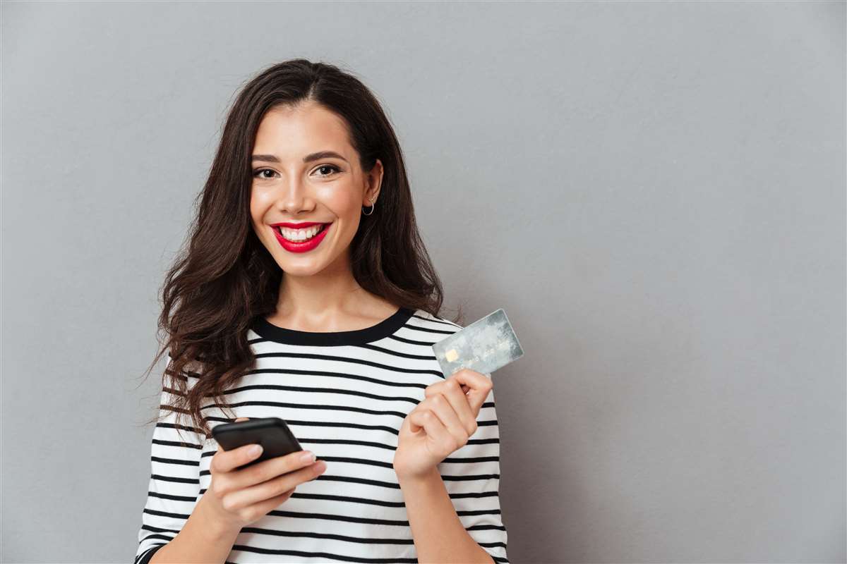 giovane donna sorridente con maglia a righe con in mano telefono e carta di credito