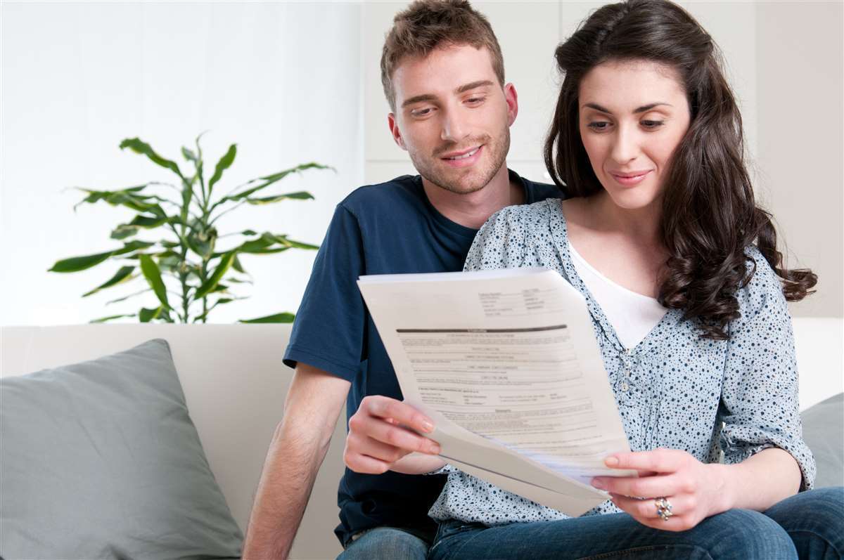giovane coppia sorridente sul divano di casa che controlla dei documenti
