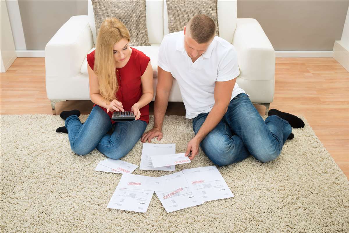 giovane coppia seduta sul tappeto davanti a tanti preventivi per aprire un conto