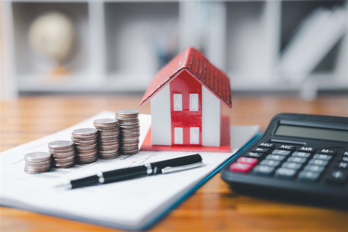 modellino di casa, pile di monete, calcolatrice e penna su scrivania