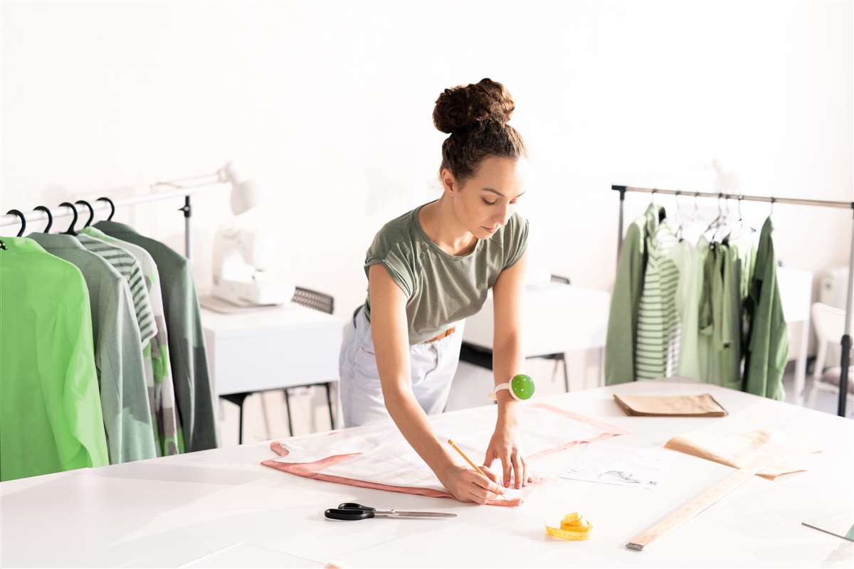 giovane donna disegna modelli di abiti su un tavolo di lavoro con alle spalle stand di vestiti