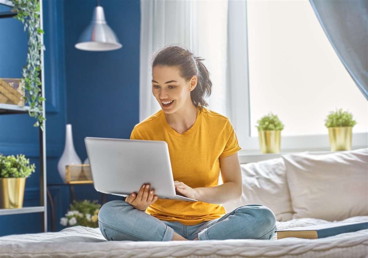 giovane donna sul divano tiene in mano un computer e guarda lo schermo sorridente