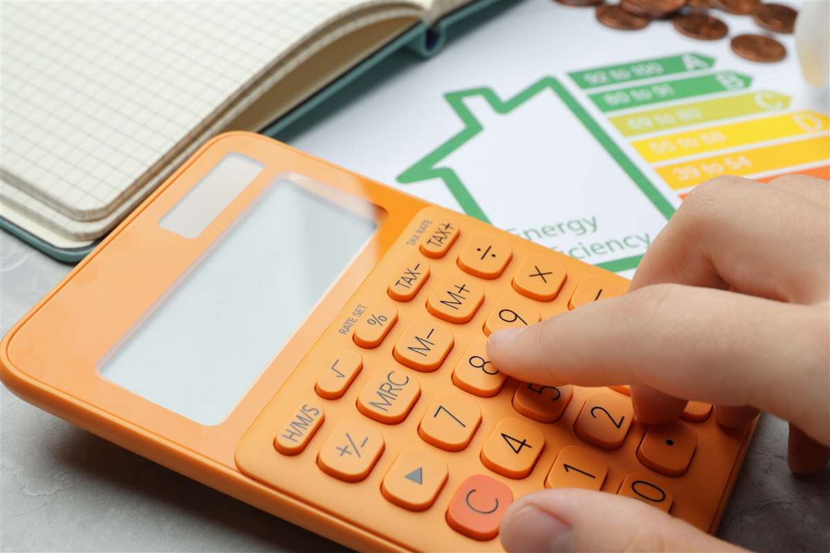 una mano digita su una calcolatrice e sullo sfondo uno schema della classe energetica