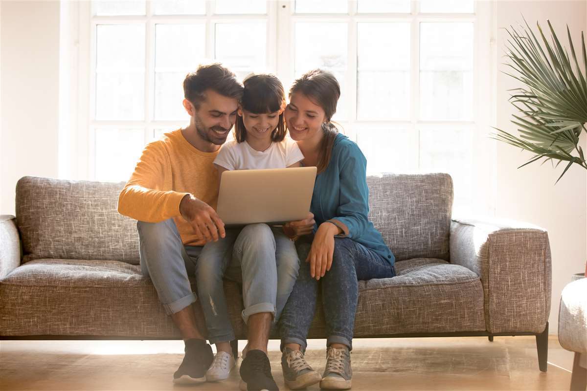 padre, madre e figlia consultano una pagina web da pc portatile seduti sul divano di casa