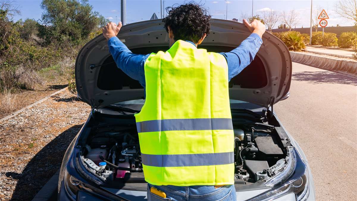 conducente con addosso giubbotto catarifrangente guarda il cofano aperto della sua auto