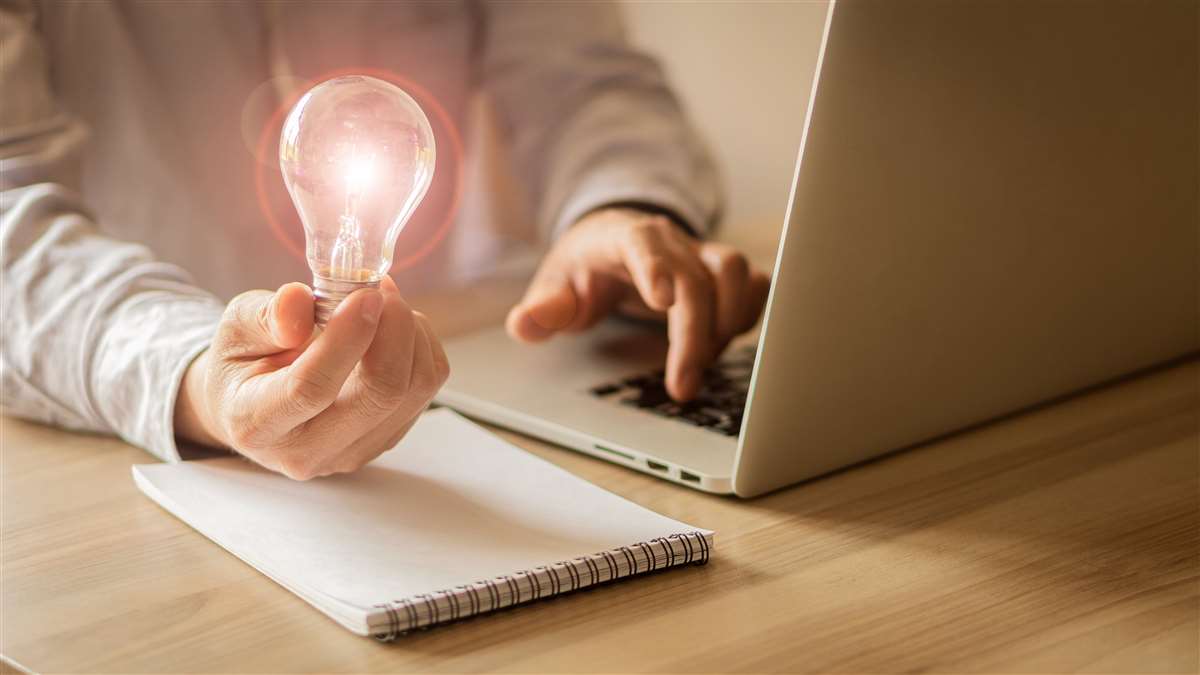 uomo al computer tiene in mano una lampadina elettrica