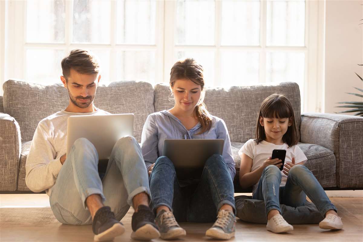 famiglia seduta per terra e ognuno con un diverso device in mano: pc, tablet e smartphone
