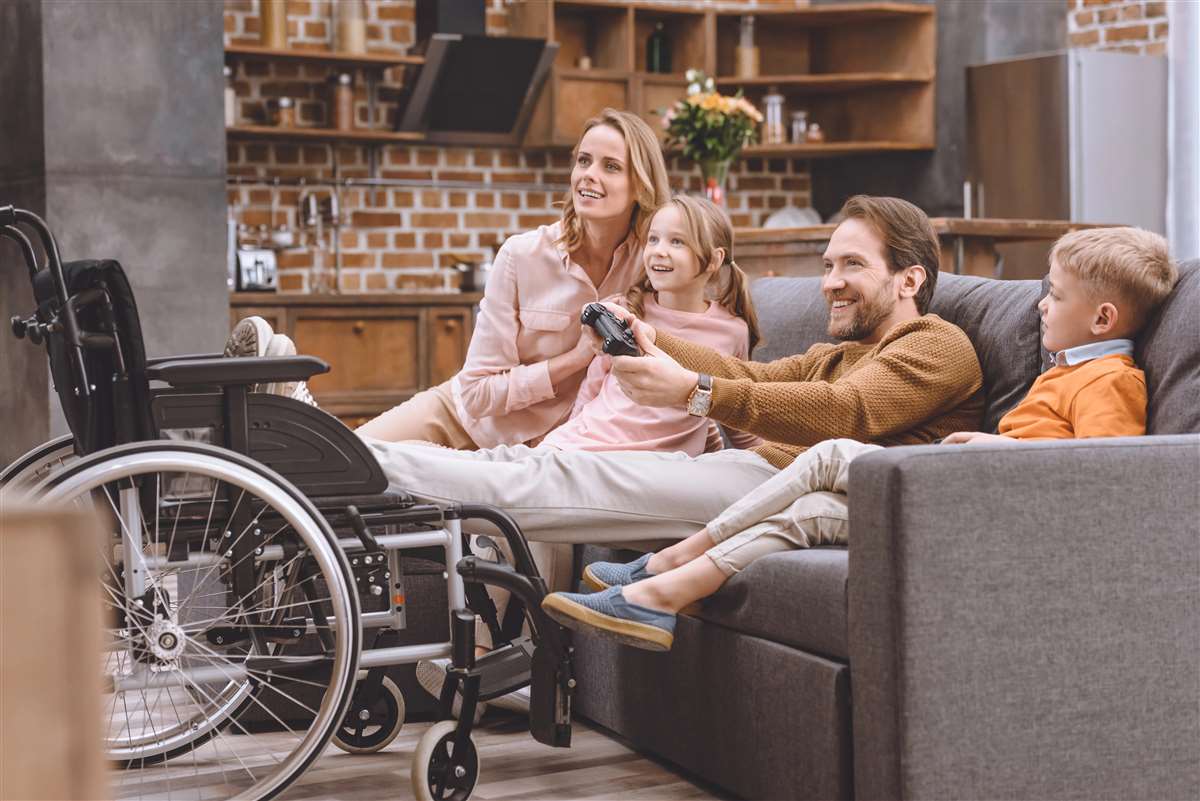 famiglia con padre disabile sorridente sul divano di casa