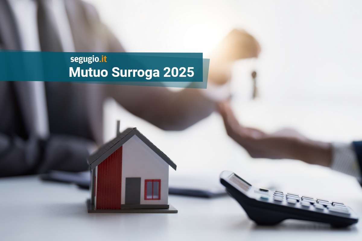 modellino di casa e calcolatrice in primo piano, sullo sfondo la consegna delle chiavi di casa