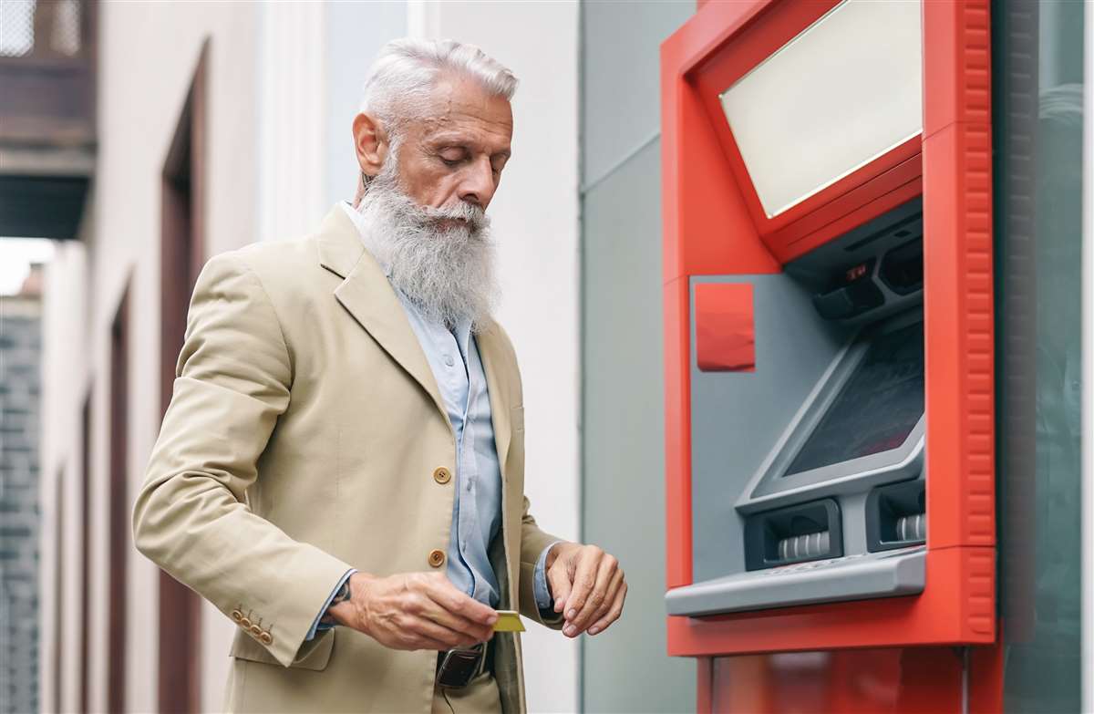 uomo anziano con barba bianca preleva denaro dal bancomat