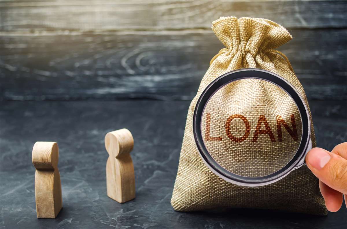 lente di ingrandimento su scritta loan posta su un sacco di juta, vicino a due sagome in legno