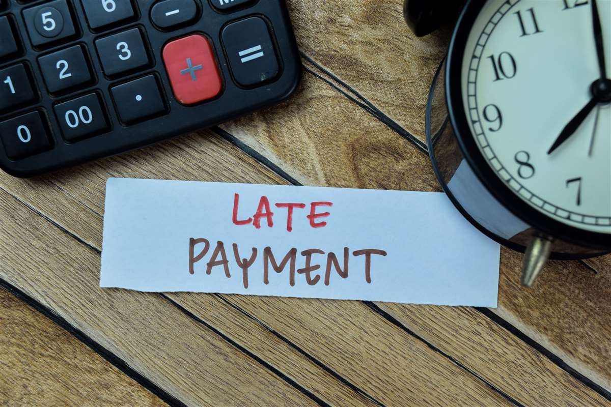 scritta late payment su foglietto vicino a calcolatrice e sveglia