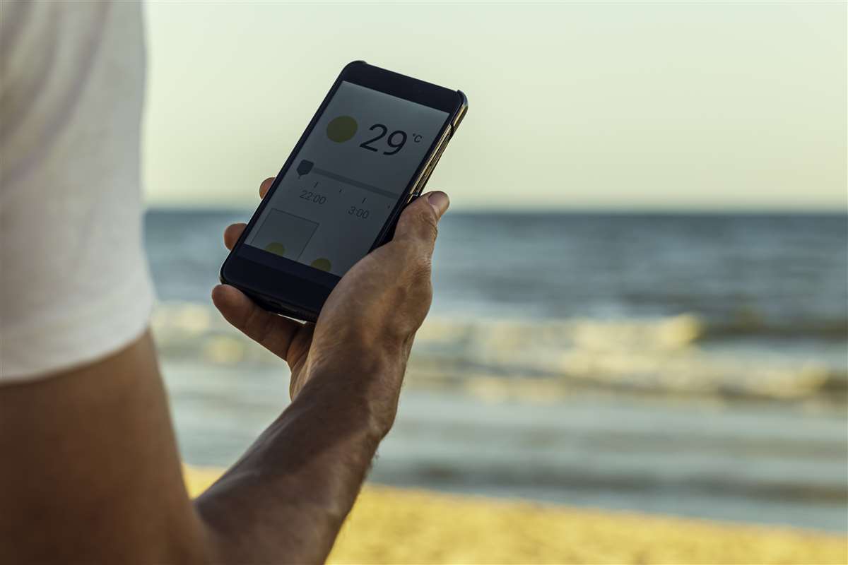 uomo controlla app meteo su smartphone in spiaggia