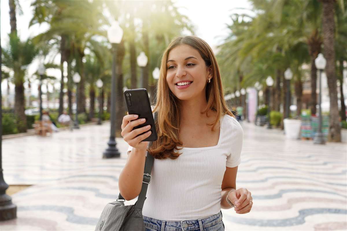 ragazza sorridente passeggia per strada con smartphone in mano