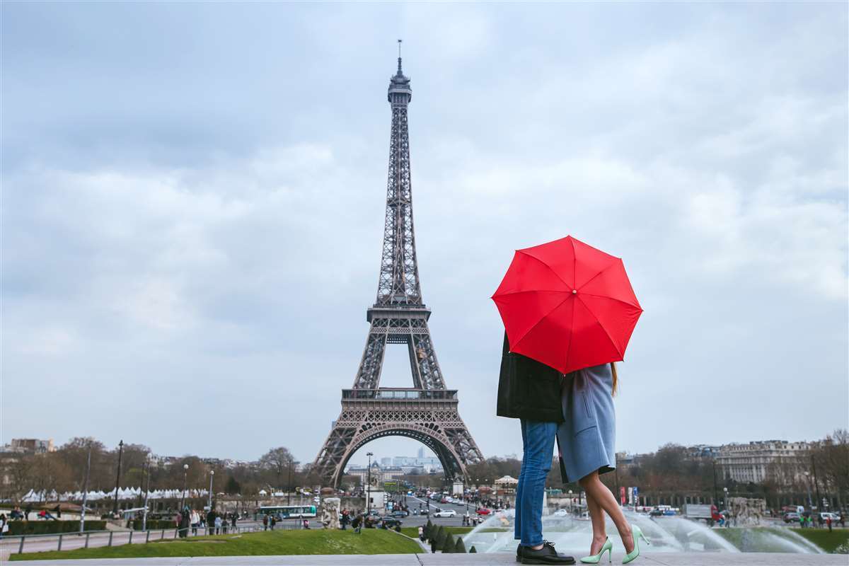 coppia si bacia dietro un ombrello rosso con torre eiffel come sfondo